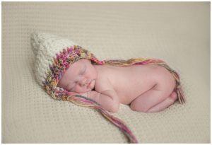 newborn baby girl wearing colourful bonnet sleeping on blanket