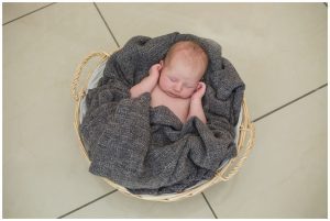 baby girl in grey blanket laid in a basket sleeping