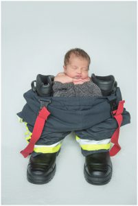 newborn baby boy posed on a blanket and firemans uniform